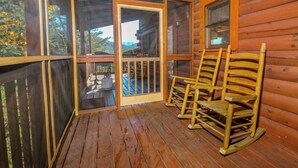 A wooden cabin with a porch, two rocking chairs, and a sliding glass door leading to an outdoor deck. - Mountain Time – 5BR Game Room & Hot Tub Cabin, Eagle Ridge Resort (Pigeon Forge)