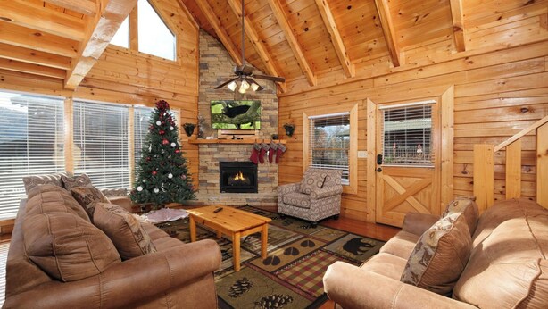 A cozy log cabin interior with a fireplace, two sofas, a coffee table, and a Christmas tree. - Mountain Time  – 5BR Game Room & Hot Tub Cabin, Eagle Ridge Resort (Pigeon Forge)