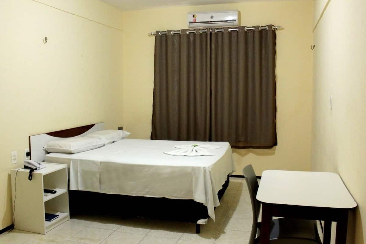A small, single-bed room with a desk and chair, a telephone, and a window with curtains.