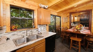 A kitchen with wooden cabinets, a double sink, and a dining area with a table set for four. - Traveler's Rest - Hot tub, pool table, and arcade games! (Pigeon Forge)