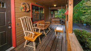 A wooden porch with rustic furniture, including a chair and a table. - Traveler's Rest - Hot tub, pool table, and arcade games! (Pigeon Forge)