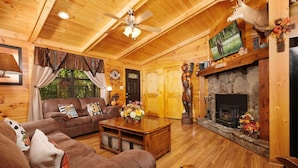 A cozy cabin interior with a wooden ceiling, a stone fireplace, a sofa, a coffee table, and a television. - Traveler's Rest - Hot tub, pool table, and arcade games! (Pigeon Forge)