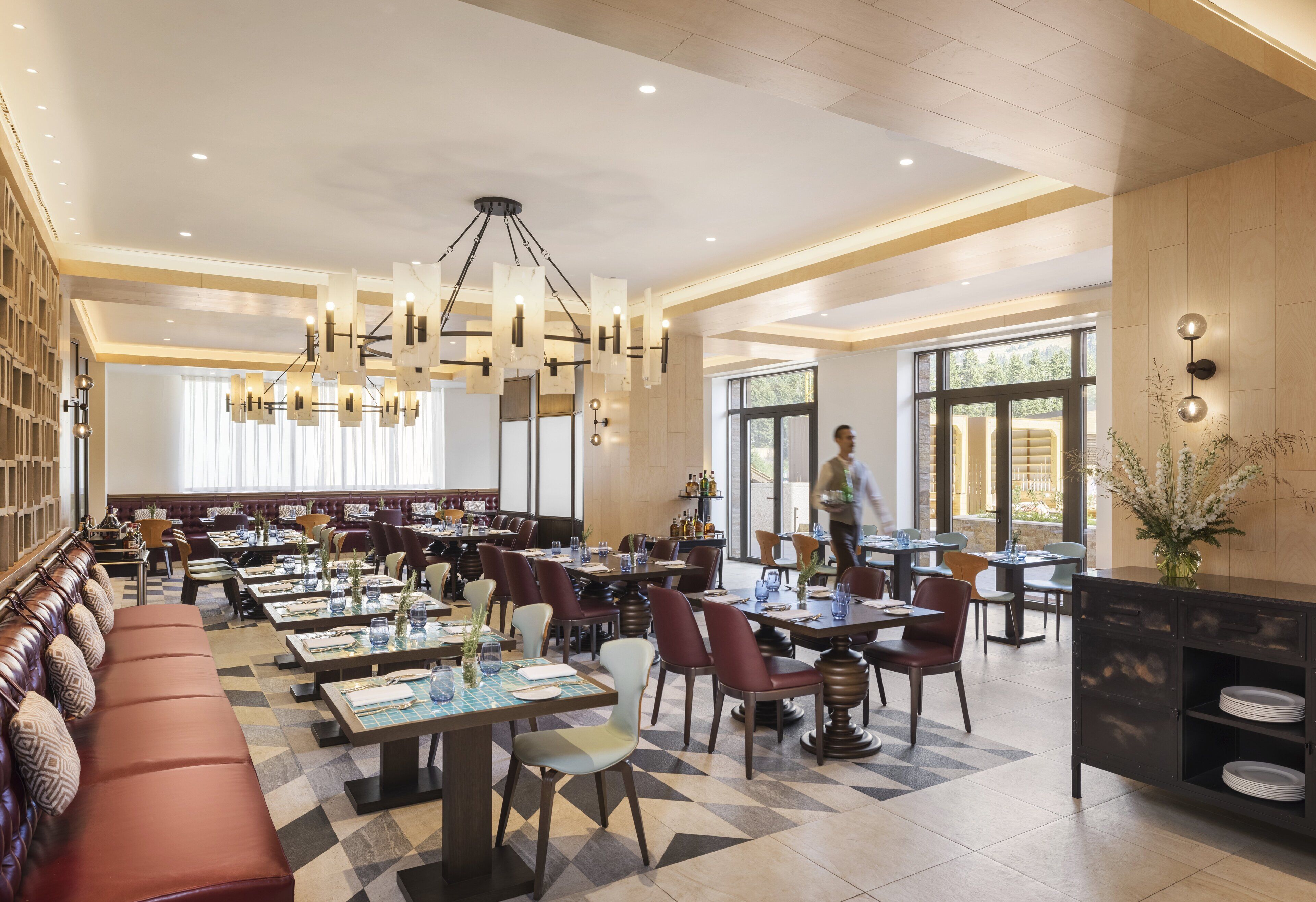A spacious restaurant with multiple dining areas, a long bench seating area, and a modern chandelier.
