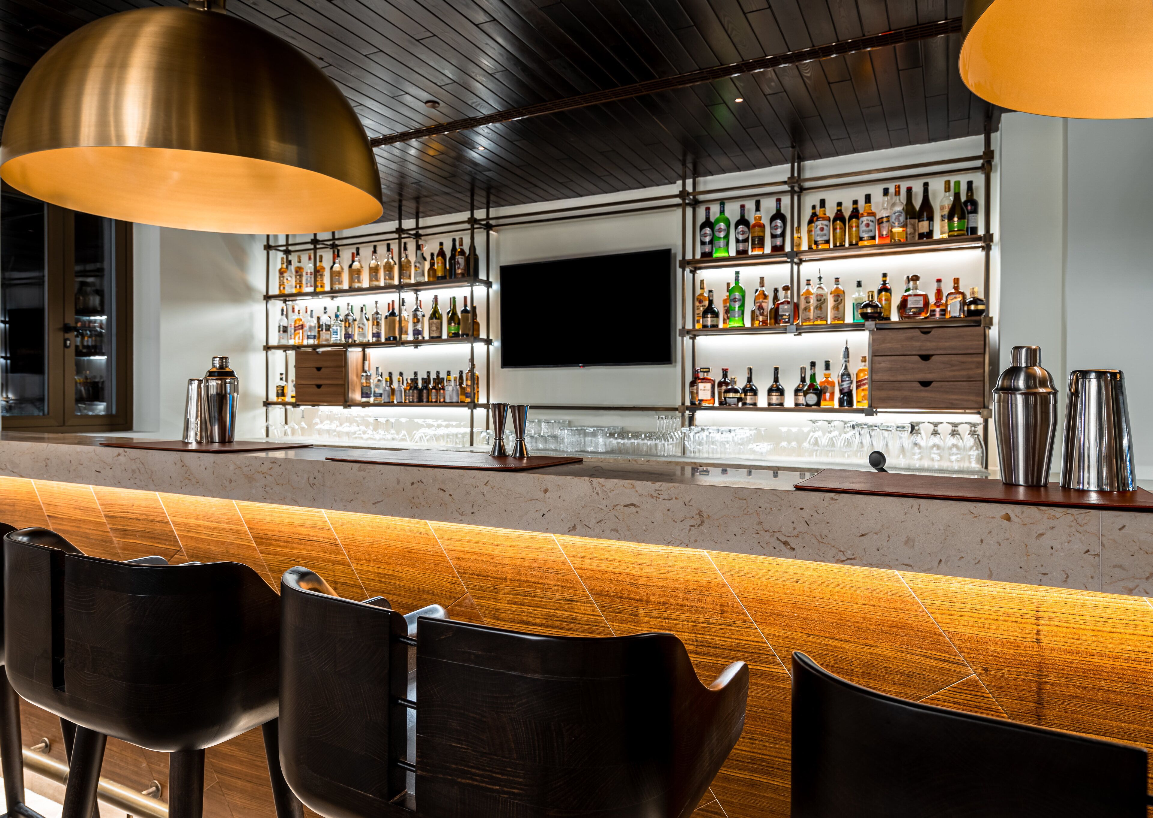 A bar area with a polished counter, multiple shelves of liquor bottles, and modern bar stools.