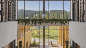 Un interior de hotel moderno con una escalera central, ventanas amplias que ofrecen vistas a un paisaje verde y un suelo con estampado de espiga.