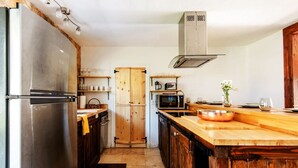 Een compacte keuken met een roestvrijstalen koelkast, houten keukenkastjes, een magnetron en een groot houten eiland met een koperen kom.