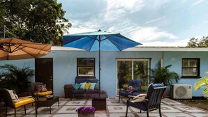 Een terras buiten met een blauwe parasol, een bank, twee stoelen en een potplant.