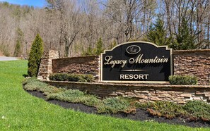 A sign for Legacy Mountain Resort with a stone wall and greenery around it.