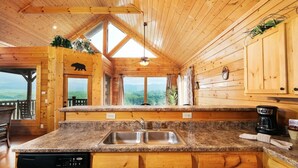 Une cuisine rustique aménagée dans une cabane en bois, avec une grande fenêtre, un évier et une machine à café.