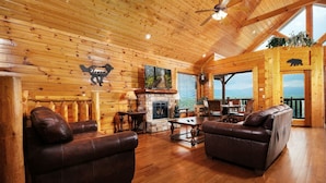 L’intérieur d’une cabane en rondins, avec une cheminée, des canapés en cuir, un plancher en bois et une vue magnifique.