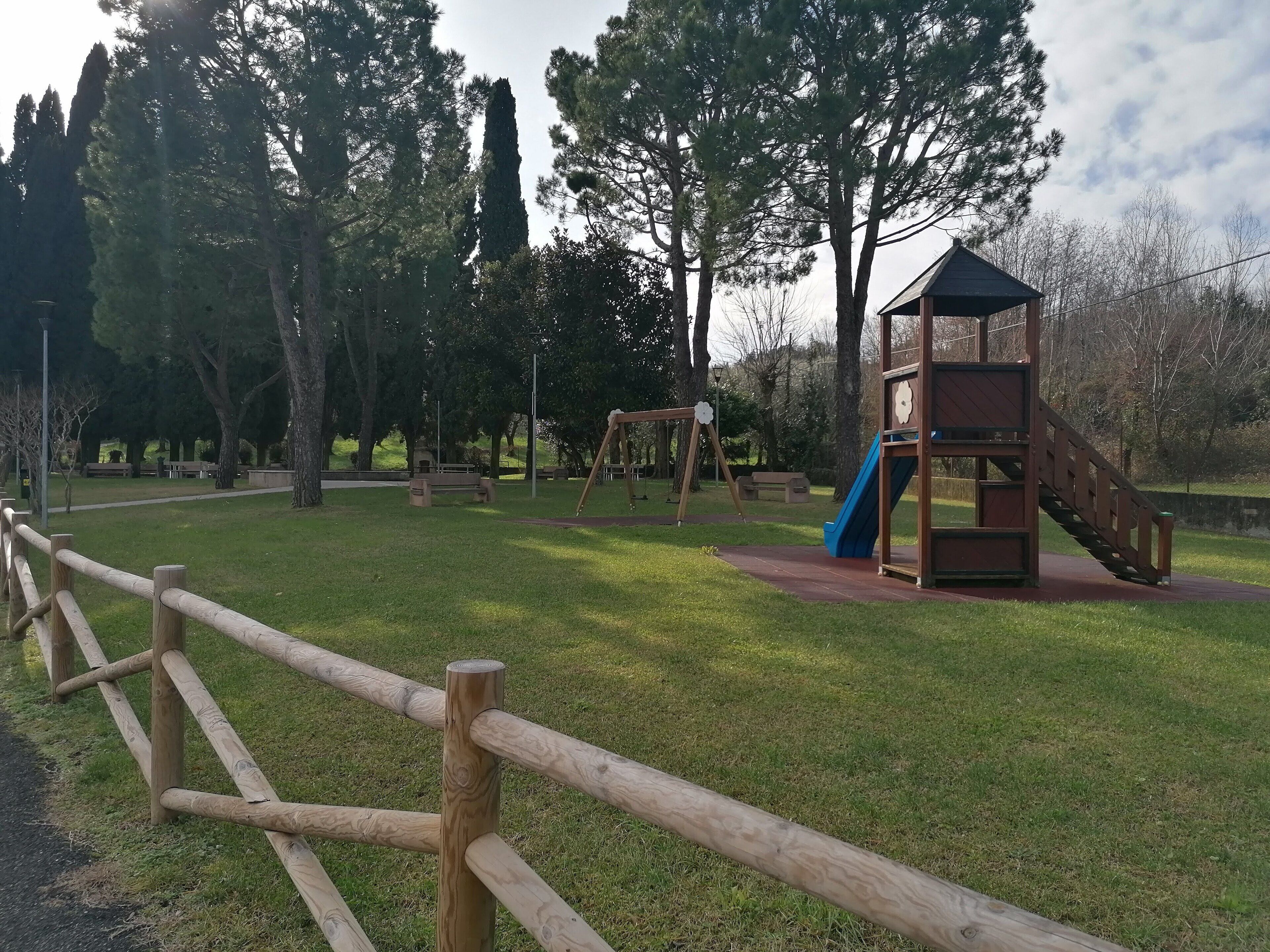 Une aire de jeux avec un toboggan et des balançoires, entourée d’arbres et d’une clôture en bois.