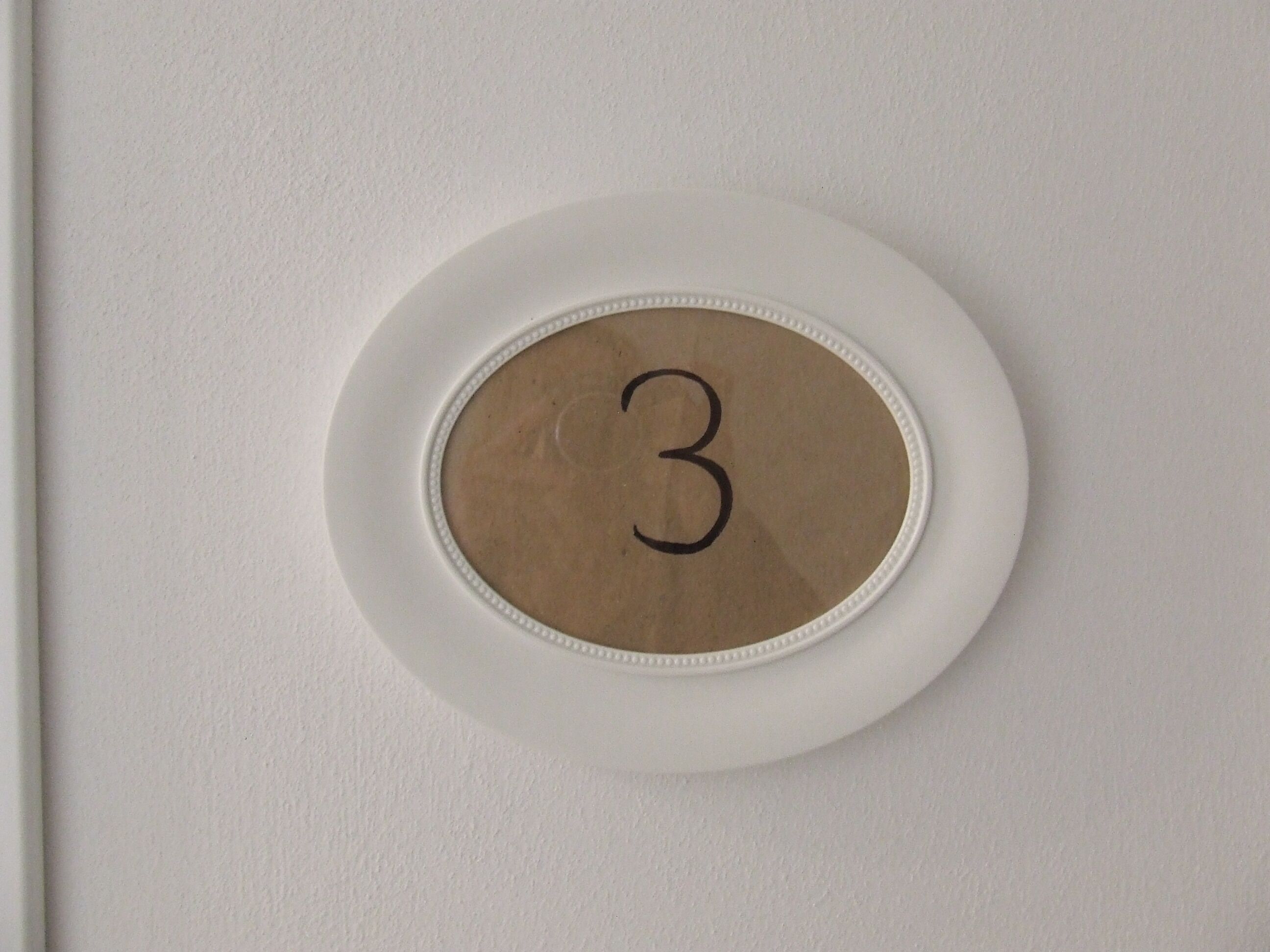 Un mur blanc sur lequel est affiché un objet circulaire portant le chiffre 3.