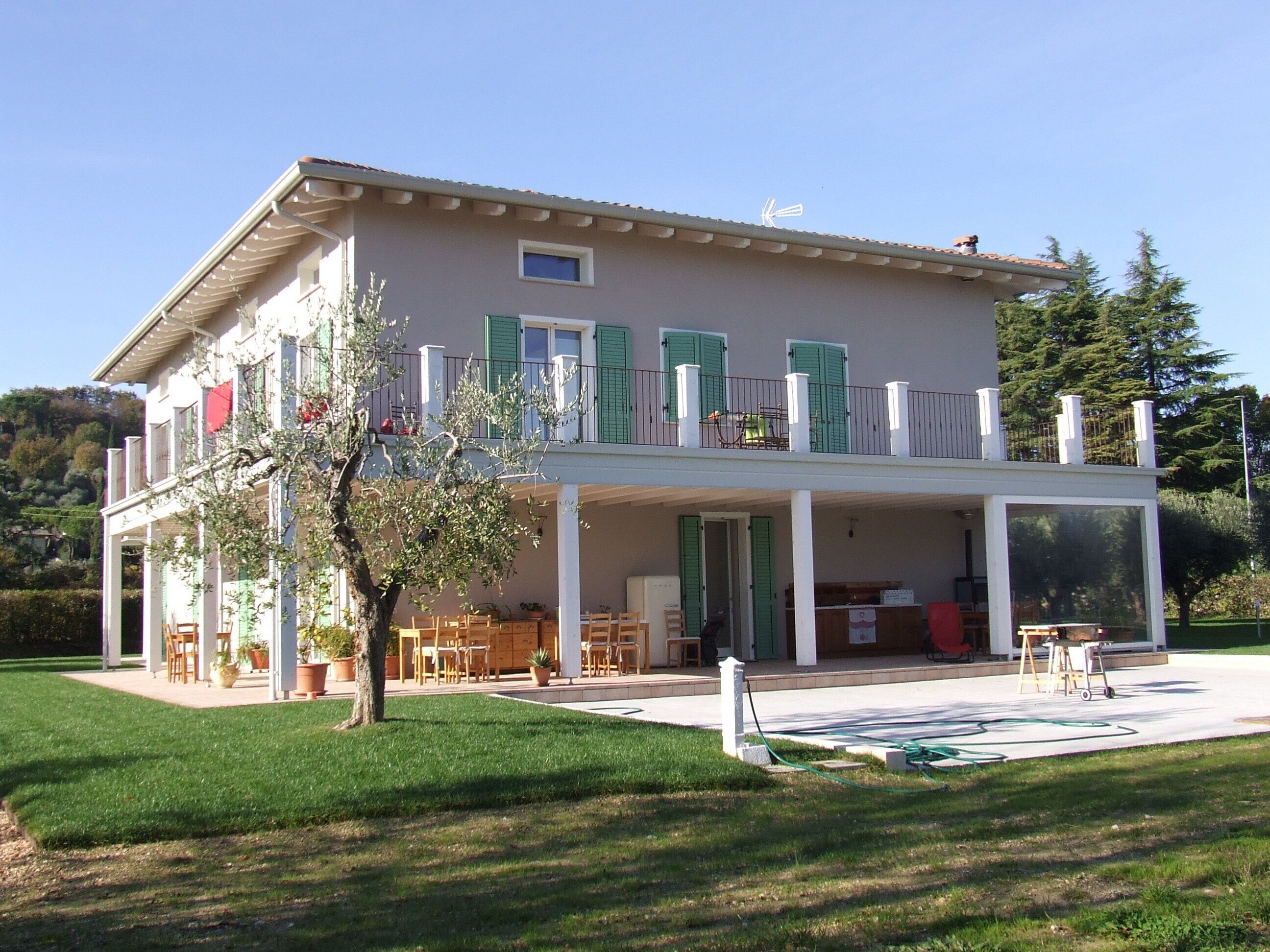 Una casa a due piani con un balcone, un portico coperto e un giardino.