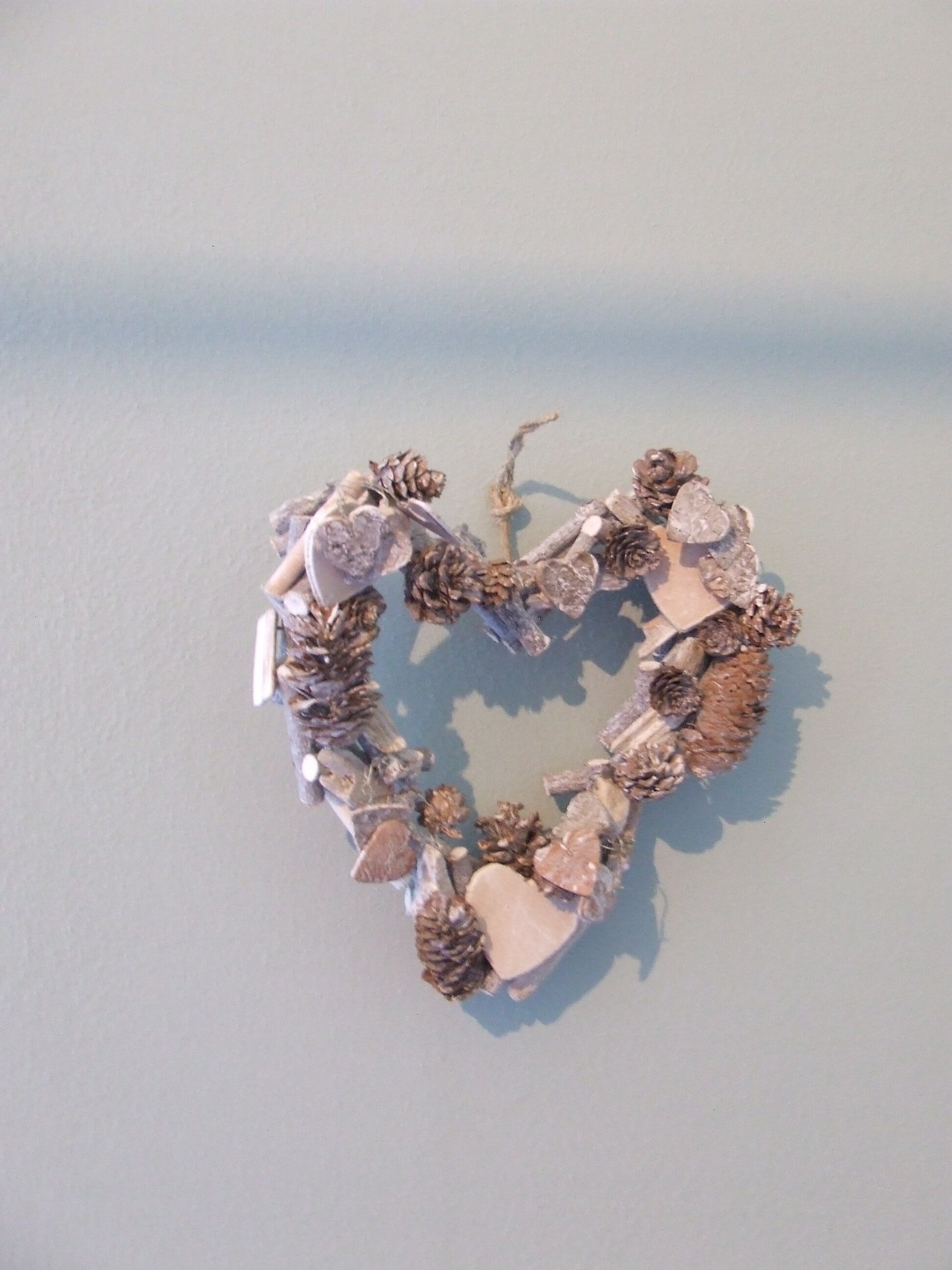 A heart-shaped decoration made of natural materials like pinecones and stones, displayed on a plain surface.