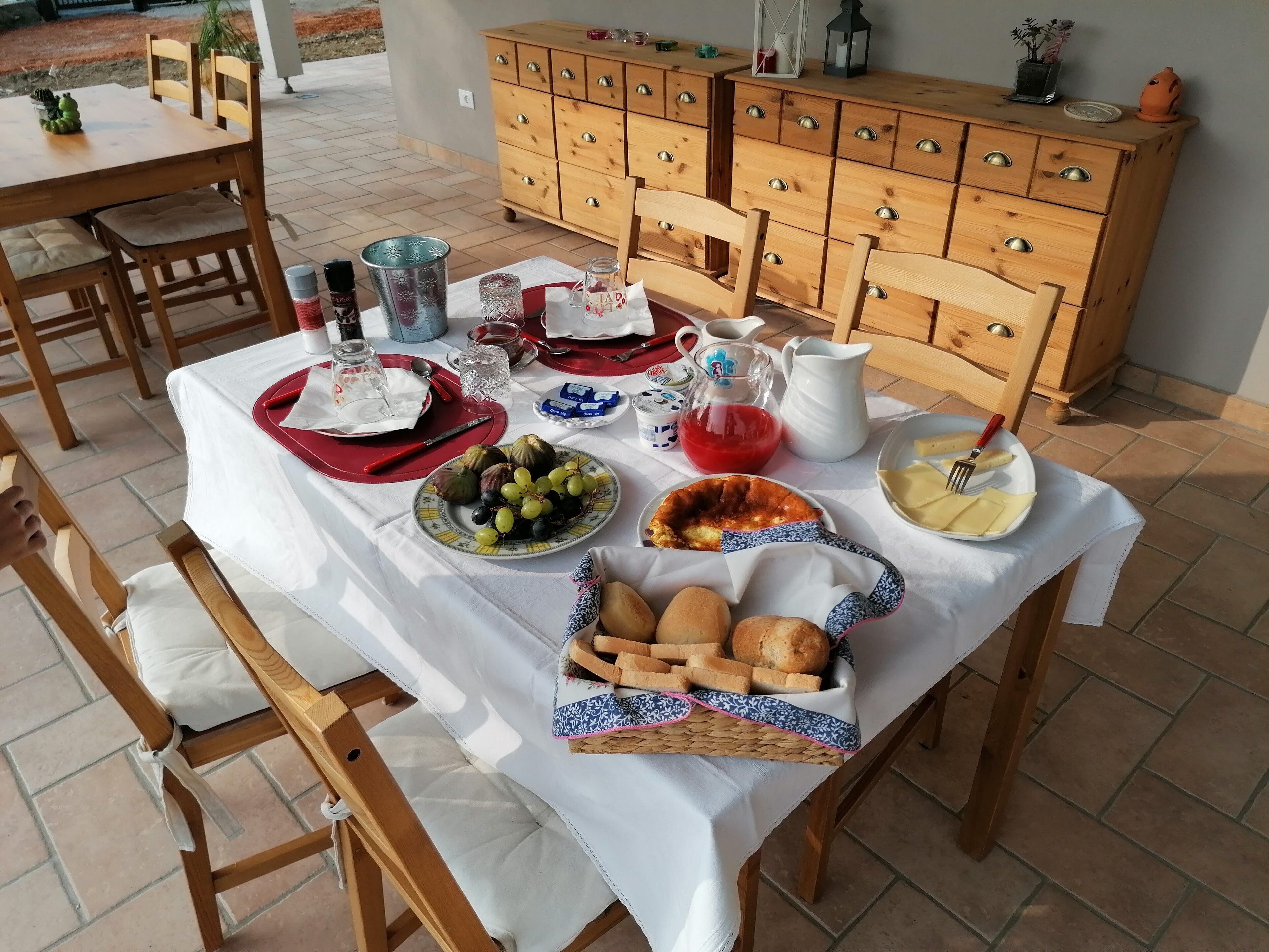 Un tavolo da pranzo all'aperto con diversi cibi, tra cui pane, frutta e una brocca d'acqua.