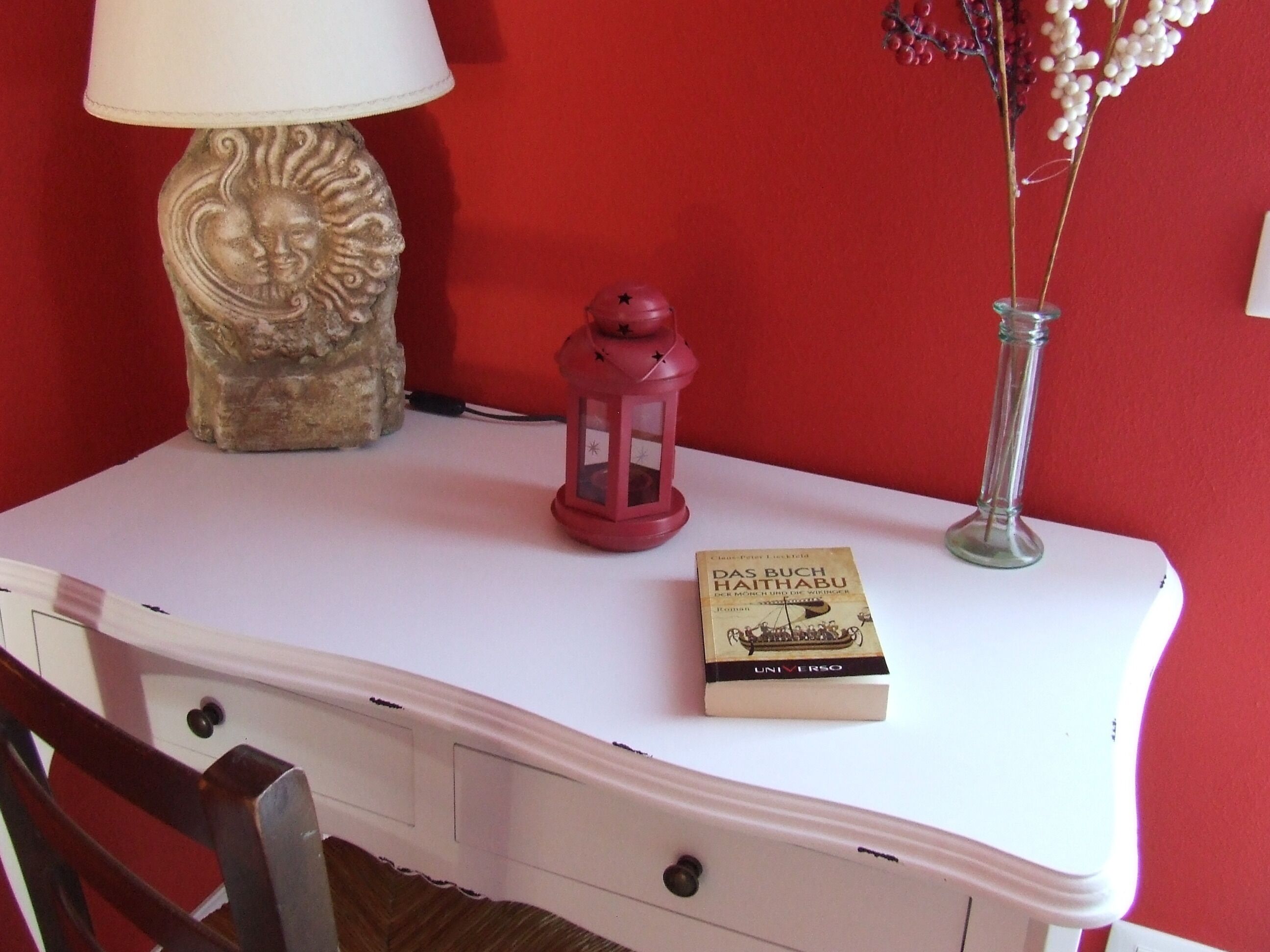 A white table with a book titled "Das Buch Haithabu" and a red lantern.