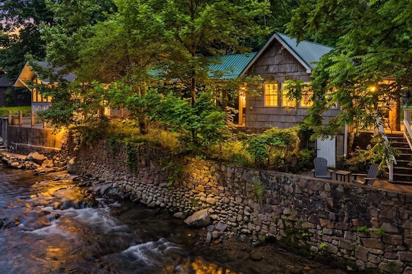 A stone wall, a wooden house with a green roof, and a flowing stream.