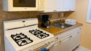 A kitchen with white cabinets, a microwave, a stove, a coffee maker, and a sink.