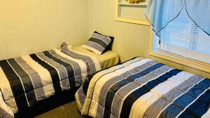 A room with two beds, each with striped bedding, a shelf with a fish decoration, and a window with blinds.