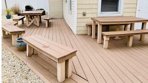 A wooden deck with picnic tables and a barbecue grill.
