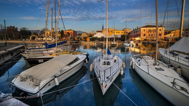 Un puerto deportivo con barcos amarrados, agua tranquila y edificios al fondo.