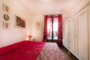 Ein Schlafzimmer mit einem Bett, einem Nachttisch, einer Lampe, einem Fenster mit Vorhängen und einem Kleiderschrank.