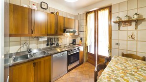 Una cocina con armarios de madera, un lavamanos de acero inoxidable, lavavajillas, horno y una mesa de comedor con sillas.