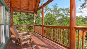 Une terrasse en bois avec une rambarde, un banc et une vue sur les arbres.