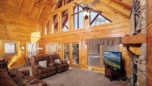 L’intérieur d’une cabane en rondins, avec une cheminée, un téléviseur et un coin salon confortable.