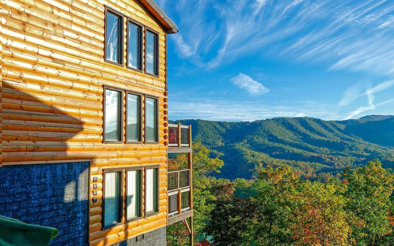 A log cabin with multiple windows and balconies, set against a backdrop of a mountainous landscape.