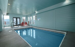 An indoor swimming pool with a view of mountains, red Adirondack chairs, and a notice board on the wall. - Point of Grace - Private Indoor Pool, hot tub, theater room, game room, mountain views, & more! (Pigeon Forge)