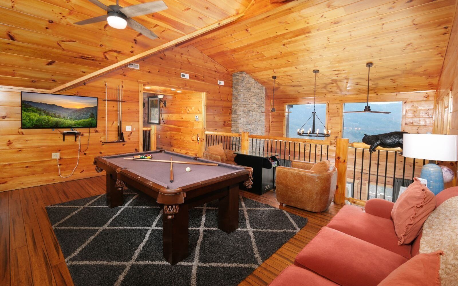 A cozy wooden cabin interior with a pool table, a sofa, and a television mounted on the wall.