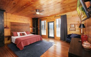 A wooden cabin bedroom with a bed, a ceiling fan, a fireplace, and a large window. - Point of Grace - Private Indoor Pool, hot tub, theater room, game room, mountain views, & more! (Pigeon Forge)