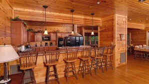 A rustic wooden cabin interior with a kitchen, bar area, and dining space.