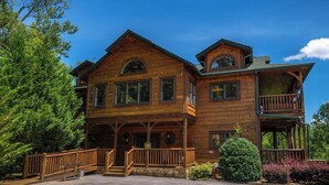 A large, two-story wooden lodge with a prominent front porch, multiple windows, and a balcony on the upper floor.