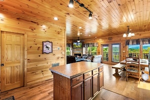 A wooden cabin interior with a kitchen area, dining space, and a fireplace. - Morning Glory - Incredible Mountain Views・Private Hot Tub, Theater, Pool Table, and Arcade! + (Gatlinburg)
