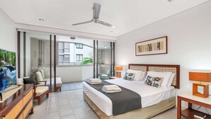 Ein modernes Hotelzimmer mit Bett, Schreibtisch, Sessel und Deckenventilator, mit Blick auf den Außenbalkon.