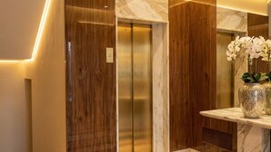 An elevator with wooden paneling and marble accents, a marble-topped console table with orchid vases, and a wall-mounted light fixture. - DesenzanoLoft Ciao Lago  (Desenzano del Garda)
