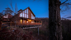 A wooden cabin with a balcony, surrounded by trees and a forested landscape.