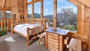 A wooden cabin room with a bed, a glass table, and a view of the forest.