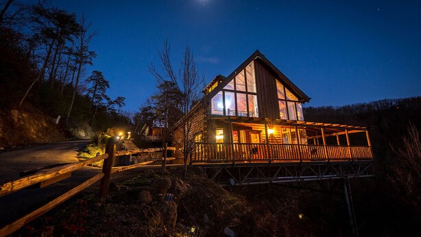 A wooden cabin with a balcony, surrounded by trees, under a night sky with a visible moon.