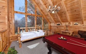 Uma cabana de madeira com cama, mesa de bilhar e uma grande janela.