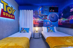 Habitación de hotel temática de Toy Story con dos camas, una mesita de noche y un mural de personajes de Toy Story.