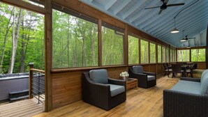 Un espacio de estar al aire libre cubierto con mobiliario de mimbre y grandes ventanales con vistas al bosque.