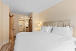 Habitación de hotel con una cama grande, puertas de madera, una mesita de noche con lámpara y un baño visible a través de una puerta abierta.