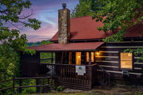 Une cabane avec une cheminée en pierre, une véranda et un panneau indiquant « Cabanes à louer ».