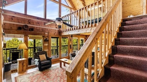 A spacious room with a high ceiling, wooden beams, a staircase, and a view of the outdoors. - Peak A View - Spectacular Mountain View, Rec Room Loft, Relaxing Hot Tub (Sevierville)