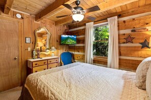 Une chambre de style cabane, comprenant un lit, une commode, un miroir, une télévision et une fenêtre avec des rideaux.