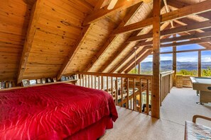 Eine Holzhütte mit einem roten Bett, einem Schreibtisch und Blick auf die Berge.