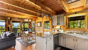A wooden cabin interior with a dining area, kitchen, and a view through the windows. - Peak A View - Spectacular Mountain View, Rec Room Loft, Relaxing Hot Tub (Sevierville)